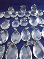 Multiple faceted teardrop shaped chandelier crystals laid out on blue fabric, showing their size and shape.