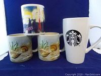 Four coffee mugs on blue background including a tall white Starbucks mug with a black logo, and three Otagiri mugs with seashell and seaweed designs.