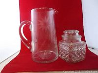 Full view of etched glass pitcher and pressed glass candy jar on red background