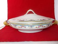 Side view of the oval serving dish with lid showing ornate floral pattern and gold-handled sides.