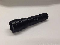 Black Ultra Fire WF-502b Cree XML LED flashlight lying on a white surface, angled to show side logo and body texture.