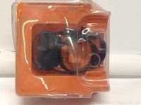 Photo of sport dog training collar in original packaging, black adjustable strap, and electronic control unit enclosed in clear plastic blister pack on an orange background.