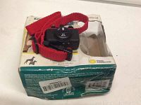 Black bark control device mounted on red adjustable collar, displayed atop original box with visible wear and tear.