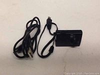 Image shows a small black digital video camera with lens, next to a USB charging cable on white background.
