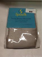 Photo of the SpaSilk Facial Beauty Pillowcase in its original packaging, featuring blue label and visible cream silk fabric inside.