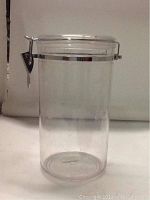 Clear cylindrical airtight canister with metal latch lid shown against white background.