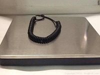 Close-up photo of the stainless steel weighing platform of the SAGA digital postal scale with connected black coiled cable.