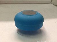 Photo showing blue waterproof shower speaker with suction cup base on a white surface