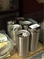 Photo of six cylindrical metal cups with brushed or polished stainless steel finish.