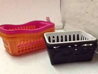 Photo showing two plastic mini home baskets: one rectangular orange and pink basket and one black and white basket with holes and woven pattern