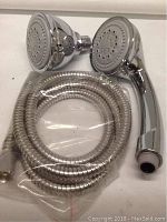 Two round shower heads and a coiled flexible hose in plastic packaging, all chrome finish.