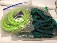 Two expandable garden hoses, one bright green and one dark green, each in sealed plastic bags.