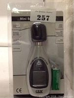 Photo of mini sound level meter in original packaging, showing front of device and included 9V battery.