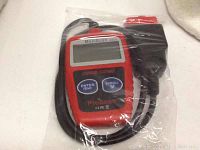 Photo showing the red and black Autel CAN OBD2 Code Scanner ProScan unit sealed in plastic, with attached cable and OBD2 vehicle connector visible.