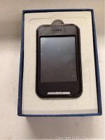 Black Pyrus Electronics media player inside a blue box with white foam insert, showing the front touchscreen and buttons.