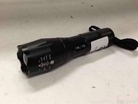 Black Ultrafire Cree XML T6 zoom flashlight with wrist strap placed on a light-colored surface.