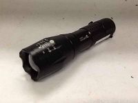 Black Ultrafire Cree XML T6 zoom flashlight on a light-colored surface.