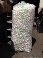 Large clear plastic bag of white packing peanuts labeled Renature, standing upright outdoors in direct sunlight.