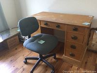 Photo showing wooden desk with nine drawers and wear marks including stains and scratches, paired with blue upholstered office chair on caster wheels.
