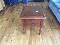 Front angled view of wooden side table showing two drawers with round metal knobs and visible scratches on tabletop.