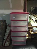 Shows two plastic storage carts stacked vertically with three translucent drawers each and pink top, placed in basement setting.