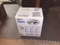Closed white Hampton Bay dehumidifier box with logo and usage instructions on a carpeted floor.