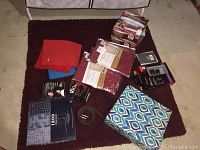 Photo shows various folded scarves in red, blue, and patterned colors, boxed Izod woven boxers, and other boxed and packaged items on a carpeted floor.