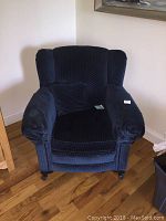 Front view of blue upholstered armchair placed on wooden floor near light-colored wall