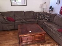 Wide view of tan sectional couch arranged around wooden coffee table with decorative pillows placed on sofa sections.
