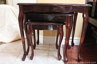 Three wooden nesting tables stacked, showing the cabriole legs and dark reddish-brown veneer finish.