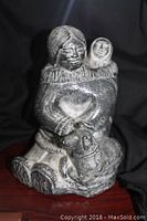 Front view of the Inuit woman carving holding a wolf with a child on her back, showing detailed facial features and clothing texture.