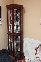 Front and side view of the full wooden curio cabinet showing the two separate glass-paneled doors, each with two glass shelves inside. The top compartment has lighting visible.