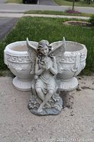 Concrete planters and resin fairy statue shown together outdoors on pavement with grass background.