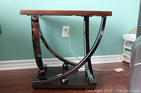 Full view of the side table showing the wooden top and metal curved base with spherical feet on wooden platform