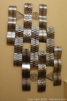 Full view of metal wall art showing all wavy and textured metal strips along with spiral and triangle accents on beige wall.