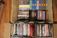 Top view of assorted DVDs stacked in plastic bins and cardboard box including DVD cases and box sets.