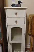 Front view of small painted wooden cabinet with two drawers above glass door