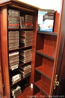Wooden shelving unit with over 150 CDs stacked and organized by spine, including jewel cases with various colored inserts and labels visible.