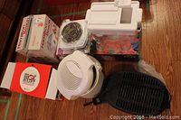 Photo showing boxed Salton electric coil cooktop, Hamilton Beach juicer, Magic Bullet blender box and base, Moulinex deep fryer, and part of punch bowl set.