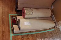 Four mats rolled and stacked by a wall and couch, includes three rubber backed mats and one jute backed runner.