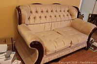 Front view of beige 2-cushion love seat with button tufted back and seat, showing scalloped carved wood exposed on top of backrest and arms.
