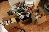 Photo showing multiple boxes containing rolls of tape, extension cords, two flashlights, party lights, and a white outdoor timer.