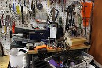Full view of workbench with vice, pliers, pruners, wrenches, screwdriver bits, mitre box, clamps, multi-tool, magnetic dish, and assorted small hand tools.
