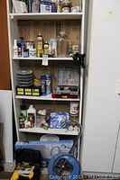White shelving unit filled with assorted hardware, household chemicals, spray cans, hand clamps, and plumbing tools