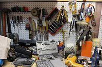 Photo of workbench showing Black and Decker drill, drill bit sets, screwdrivers, and various hand tools against pegboard.