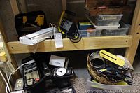 Tools and accessories on wooden shelving including nailer, light, plastic hardware bins, and fabric case with tool bits.