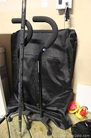 Two small base quad canes standing upright, one with a carved duck handle and decorative shaft, the other with a padded black handle.