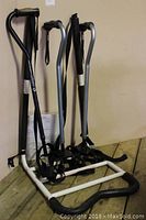 Photo showing three quad canes in black, silver, and black with white shaft, alongside a white metal M Rail bed support frame with black padded legs, leaning against a beige wall