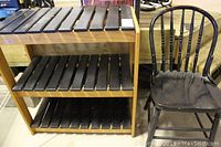 Wooden slat shelf unit with three levels and black wooden hoop back chair beside it, both show signs of wear.