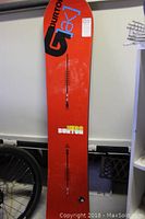Full view of the Burton AK Hero snowboard showing the red base with black and blue Burton AK logo graphics.